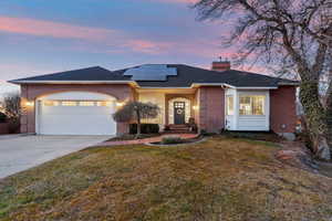 Ranch-style home with a garage, a lawn, and solar panels