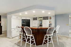 Kitchen with light colored carpet, a breakfast bar, white cabinets, and black fridge