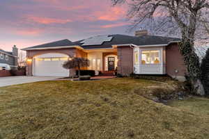 View of front facade featuring a garage, a lawn, and solar panels