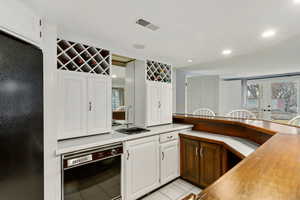 Kitchen featuring sink, light tile patterned floors, black appliances, and white cabinets