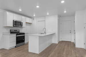 Kitchen with sink, white cabinets, kitchen peninsula, stainless steel appliances, and light hardwood / wood-style flooring