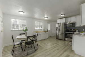 Kitchen featuring appliances with stainless steel finishes, white cabinetry, backsplash, light hardwood / wood-style floors, and a textured ceiling