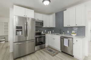 Kitchen with sink, light hardwood / wood-style floors, white cabinets, and appliances with stainless steel finishes