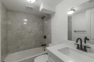 Full bathroom featuring vanity, toilet, tiled shower / bath combo, and a textured ceiling