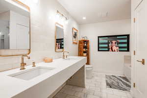 Bathroom featuring decorative backsplash, toilet, sink, and a bath