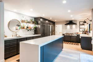 Kitchen with sink, a center island, light hardwood / wood-style floors, stainless steel gas cooktop, and wall chimney exhaust hood