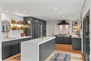 Kitchen with a kitchen island, stainless steel gas stovetop, sink, wall chimney range hood, and light wood-type flooring