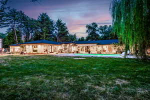 Back house at dusk featuring a lawn and a patio area