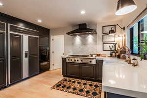 Kitchen featuring wall chimney exhaust hood, light hardwood / wood-style floors, paneled built in fridge, decorative backsplash, and stainless steel gas stovetop