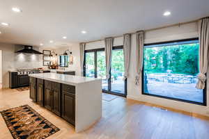 Kitchen with tasteful backsplash, a kitchen island, wall chimney exhaust hood, and light wood-type flooring