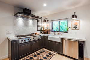 Kitchen with appliances with stainless steel finishes, tasteful backsplash, sink, wall chimney range hood, and light hardwood / wood-style flooring