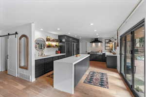 Kitchen with a kitchen island, sink, a barn door, light wood-type flooring, and wall chimney exhaust hood