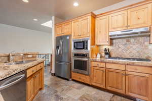 Kitchen featuring stainless steel appliances, light stone countertops, sink, and backsplash