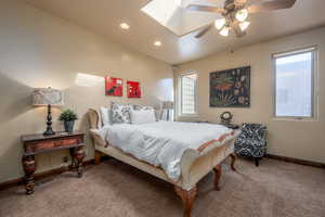 Carpeted bedroom with vaulted ceiling with skylight and ceiling fan