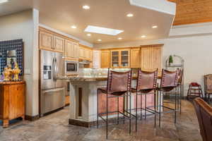 Kitchen featuring a breakfast bar, a skylight, stainless steel appliances, light stone counters, and tasteful backsplash