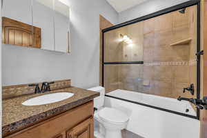 Full bathroom with vanity, shower / bath combination with glass door, and toilet