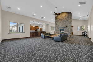 Living room featuring dark colored carpet, ceiling fan, a fireplace, and high vaulted ceiling