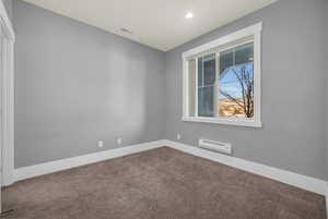 Carpeted spare room featuring a baseboard heating unit