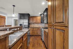 Kitchen with sink, hanging light fixtures, appliances with stainless steel finishes, dark hardwood / wood-style flooring, and decorative backsplash