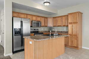 Kitchen featuring stainless steel appliances, an island with sink, sink, and a textured ceiling