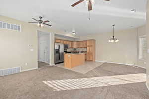 Kitchen featuring hanging light fixtures, a center island with sink, light colored carpet, stainless steel appliances, and ceiling fan with notable chandelier