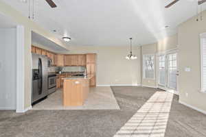 Kitchen with sink, decorative light fixtures, a center island with sink, light colored carpet, and stainless steel appliances