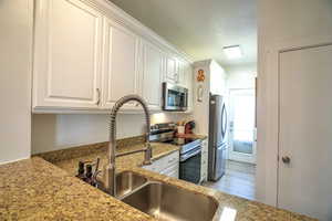 Kitchen with stainless steel appliances, sink, white cabinets, and light stone counters