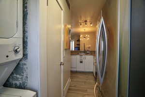 Kitchen featuring white cabinetry, stainless steel fridge, stacked washer / drying machine, white dishwasher, and light hardwood / wood-style flooring