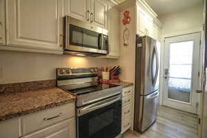 Kitchen with white cabinetry, stainless steel appliances, light hardwood / wood-style floors, and dark stone counters