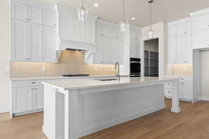 Kitchen featuring decorative light fixtures, stainless steel gas cooktop, a center island with sink, and white cabinets