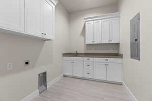 Clothes washing area with electric dryer hookup, sink, electric panel, and cabinets