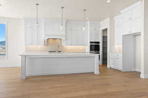 Kitchen featuring an island with sink, sink, and white cabinets