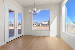 Unfurnished dining area with an inviting chandelier, french doors, and light wood-type flooring