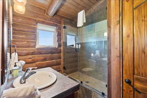 Bathroom with vanity, log walls, a shower with shower door, and wooden ceiling