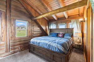 Carpeted bedroom with vaulted ceiling with beams, log walls, and wooden ceiling