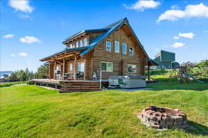 Rear view of house featuring a fire pit, a yard, a wooden deck, a hot tub, and a playground