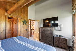 Bedroom featuring light carpet, beamed ceiling, and wood walls