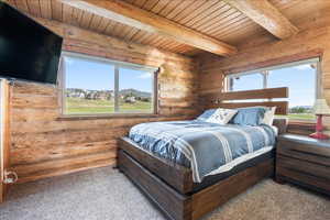 Bedroom with light colored carpet, beam ceiling, rustic walls, and multiple windows