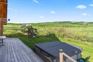 Wooden terrace with a rural view, a lawn, a covered hot tub, and a playground