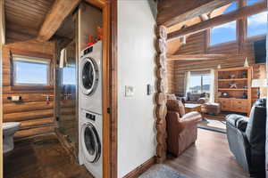 Washroom featuring stacked washer and dryer, wood-type flooring, and rustic walls