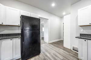 Kitchen featuring black refrigerator, dark stone countertops, white cabinets, and light hardwood / wood-style flooring