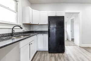 Kitchen featuring black refrigerator, sink, dark stone counters, and white cabinets