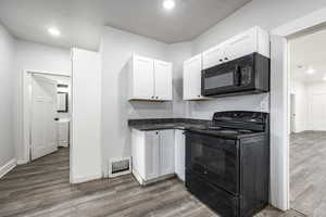 Kitchen featuring white cabinetry, dark hardwood / wood-style flooring, and black appliances