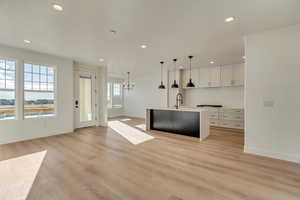 Kitchen with decorative light fixtures, light hardwood / wood-style flooring, an island with sink, and white cabinets