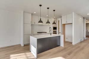 Kitchen with appliances with stainless steel finishes, white cabinetry, sink, hanging light fixtures, and a kitchen island with sink