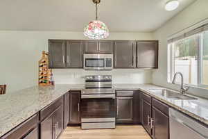 Kitchen with appliances with stainless steel finishes, sink, hanging light fixtures, light stone countertops, and light hardwood / wood-style flooring