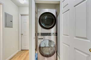 Washroom with stacked washer and dryer, light hardwood / wood-style flooring, and electric panel