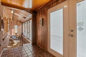 Doorway to outside with lofted ceiling, wood ceiling, dark tile patterned floors, and wood walls