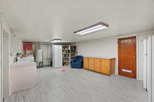 Interior space with water heater, light wood-type flooring, white refrigerator, and washer / clothes dryer