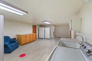 Clothes washing area with washer / clothes dryer, sink, and light wood-type flooring